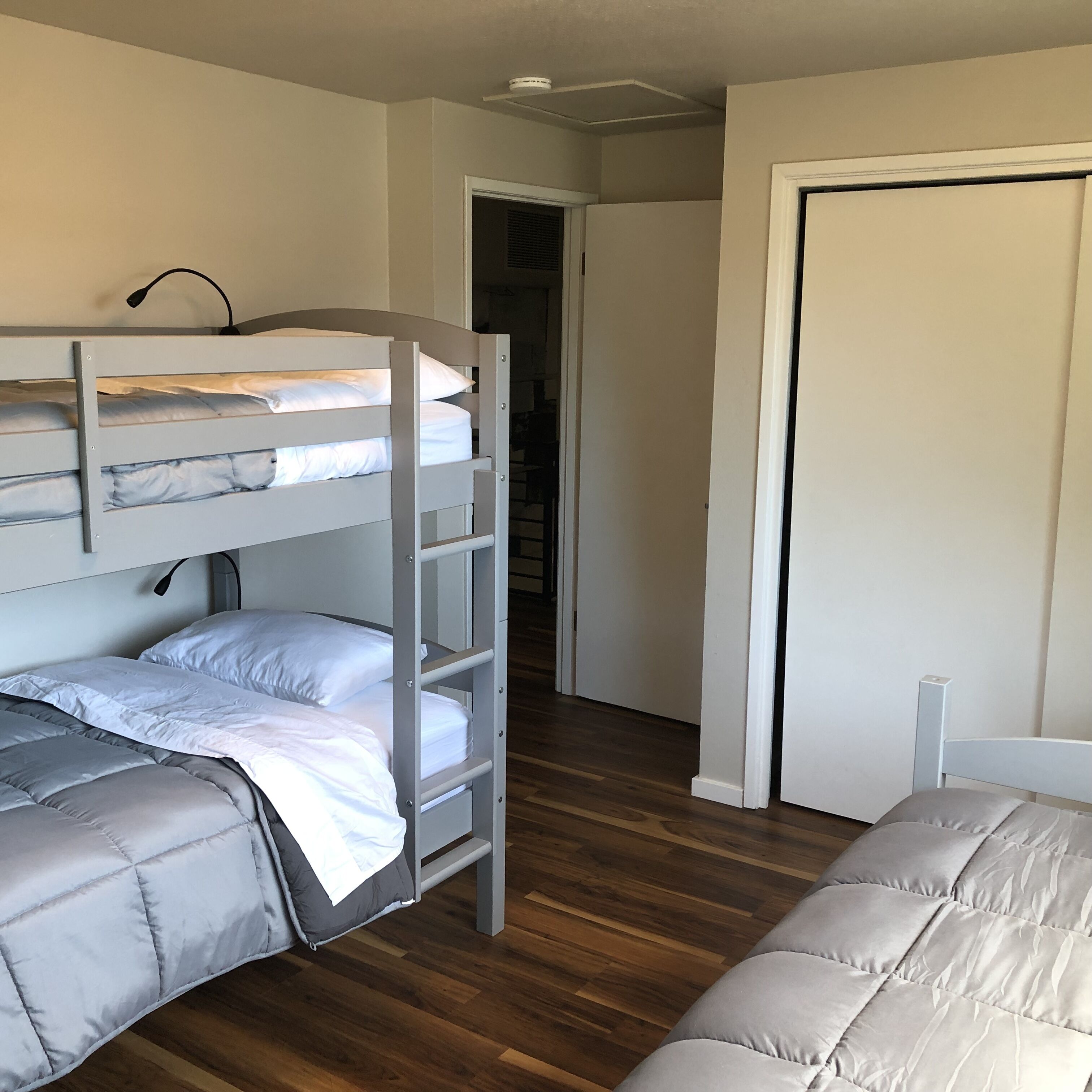 A bunk bed room with a wooden floor, a white door, and a white wall.