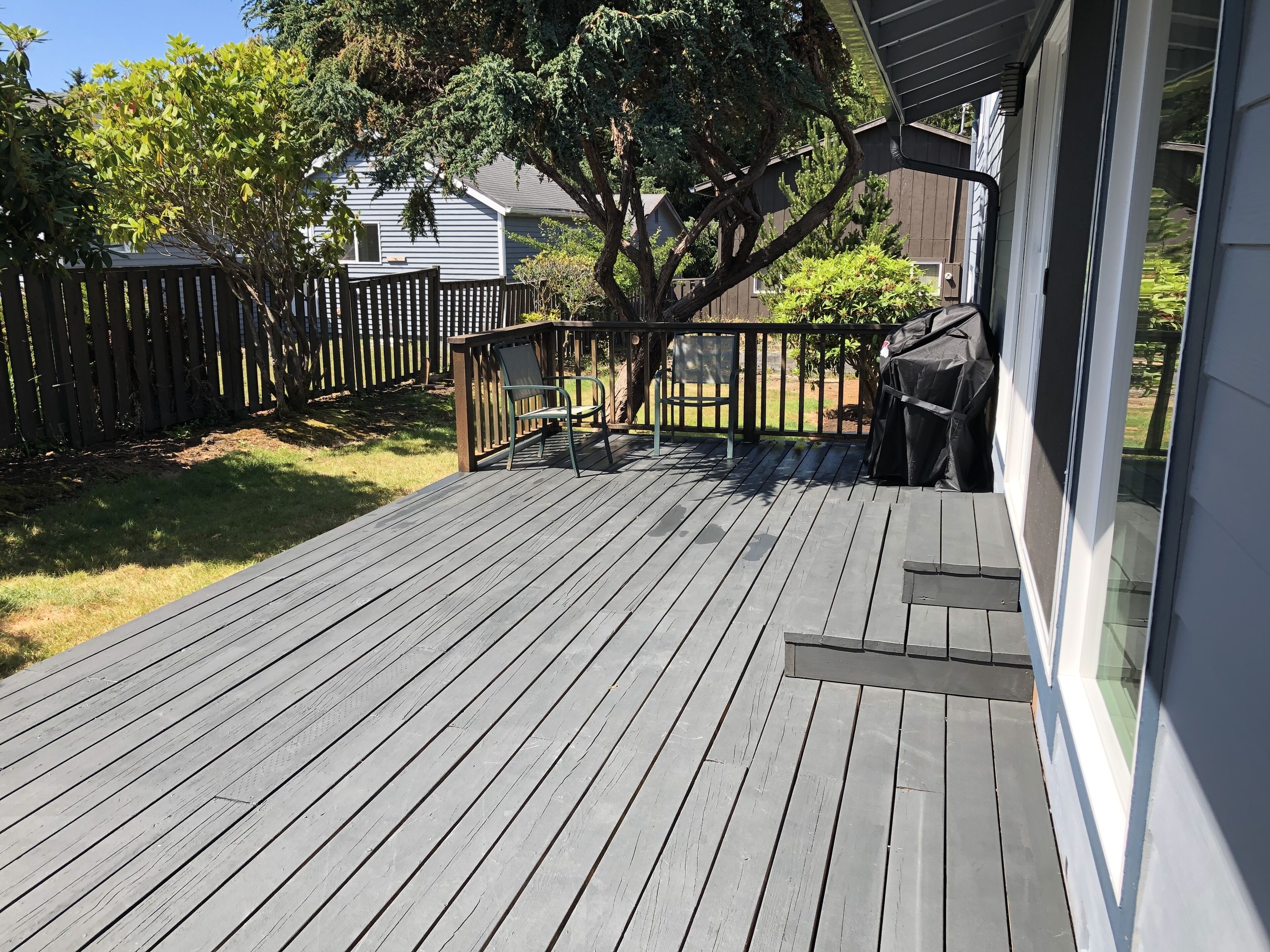 A wooden deck with a railing, a covered grill area, and a view of a residential building in the background.