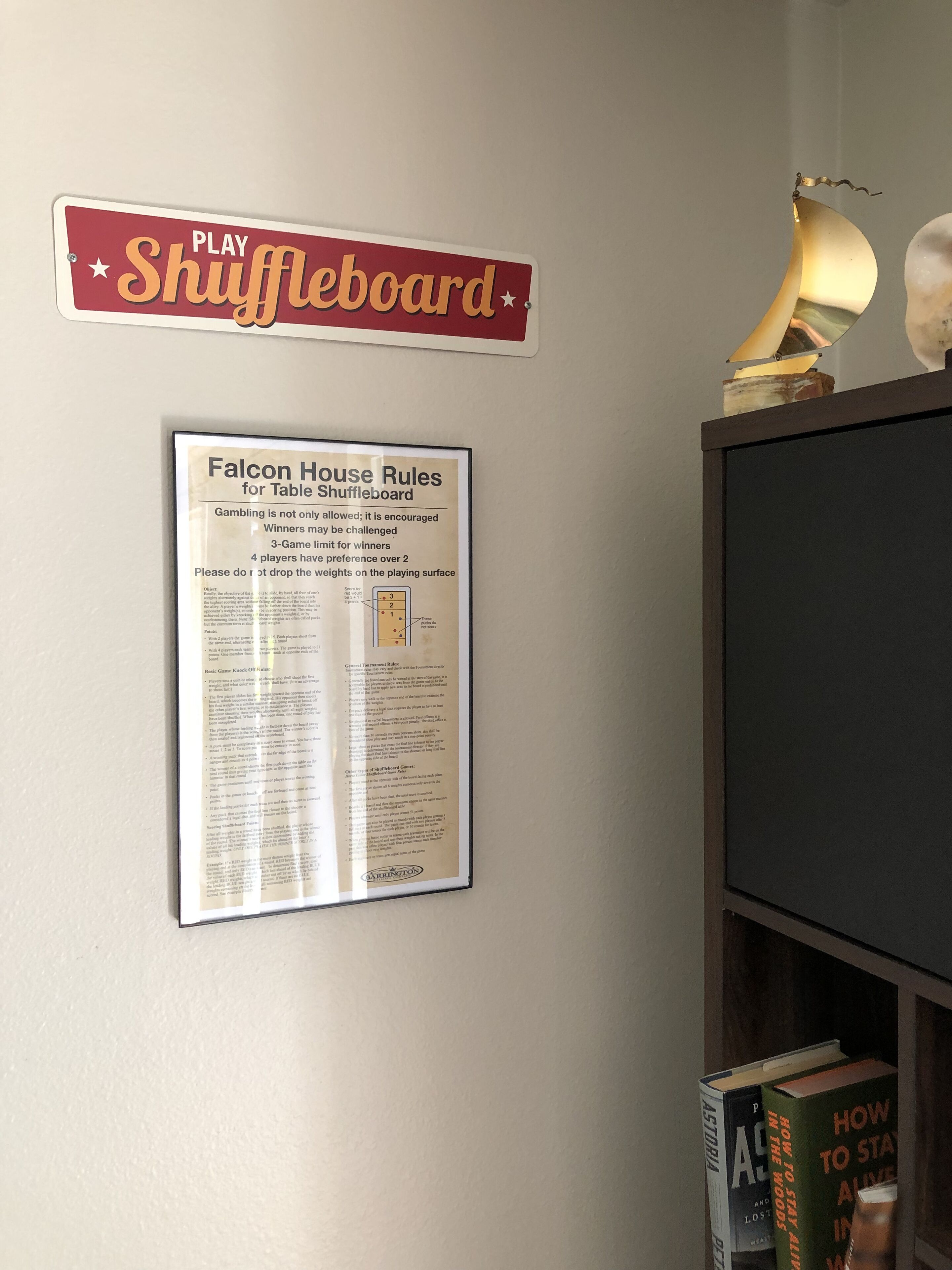 Un mur avec une pancarte indiquant « Aire de jeu de shuffleboard » et une affiche intitulée « Règles de la maison Falcon pour le shuffleboard ».