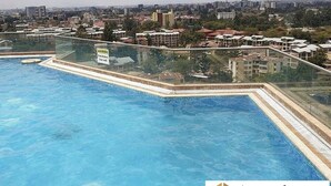 A swimming pool with a glass barrier, surrounded by buildings and a clear sky.