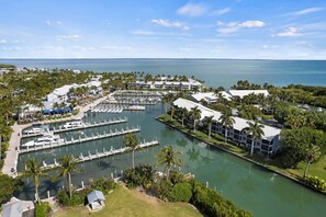 Un puerto deportivo con barcos amarrados, un edificio de marina y un hotel con piscina y palmeras.