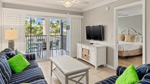 Una habitación con sofá, mesa, televisión, balcón con sillas y cama.
