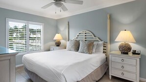 Un dormitorio con cama, dos mesitas de noche, ventilador de techo y ventana con persianas.