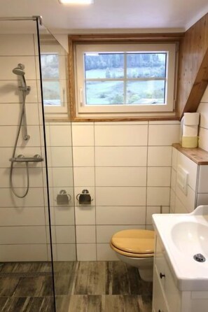 Ein Badezimmer mit Dusche, Toilette und einem Fenster über dem Waschbecken.