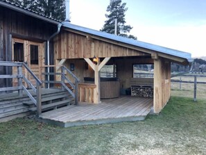 A wooden cabin with a covered porch, a hot tub, and a staircase leading to the entrance.
