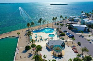 Luftaufnahme eines Resorts mit großem Schwimmbad, Palmen und Strand.