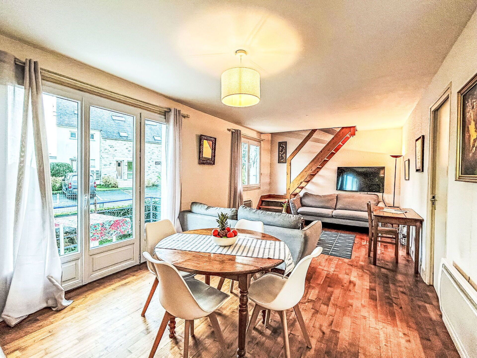Un salon chaleureux comprenant un coin repas, un escalier et de grandes fenêtres.