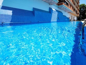 A swimming pool with clear blue water, a tiled edge, and a building with balconies in the background. - Apartment Eureka by Interhome (Malgrat de Mar)