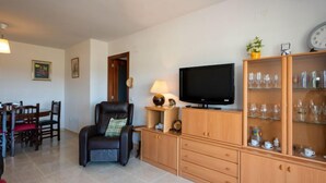 A living room with a leather chair, a television, wooden cabinets, and a dining area with chairs and a table.