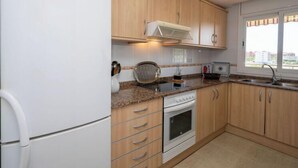 A compact kitchen with wooden cabinets, a white refrigerator, a stove, and a window with a view of buildings.