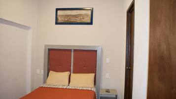 A bedroom with a bed, a nightstand, a framed picture on the wall, and a wooden door.