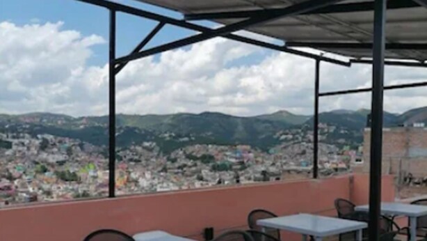 An outdoor patio with tables and chairs, a covered area, and a view of a cityscape and mountains in the background. - Hotel Casa Autora 40 (Guanajuato)
