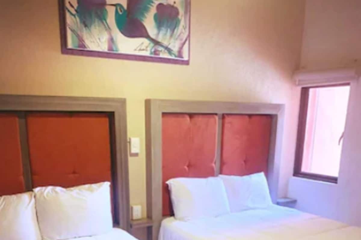 A hotel room with two beds, each with a headboard and white bedding.