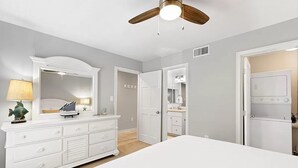 Een slaapkamer met een groot bed, een dressoir, een spiegel, een plafondventilator en een inloopkast.