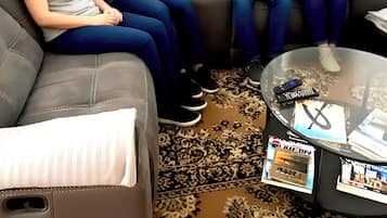 A living room with a grey sofa, a glass coffee table with magazines, and a patterned rug.