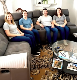 A living room with a grey sofa, a glass coffee table with magazines, and a patterned rug.