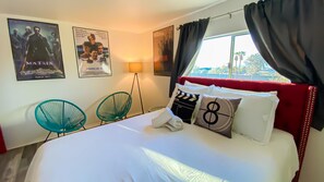 Een hotelkamer met een groot bed, twee groene stoelen, een rode hoofdbord en filmposters aan de muur.