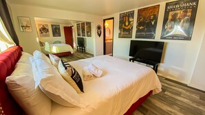 A hotel room with a large bed, a TV, and posters on the wall. - Stylish Desert Retreat - Stunning Views, 3 Min to Joshua Tree Park (Twentynine Palms)