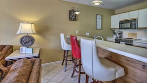 A compact kitchen with a microwave, stove, and bar stools. - Osage Beach Condo w/ Shared Pool & Lake Views! (Osage Beach)