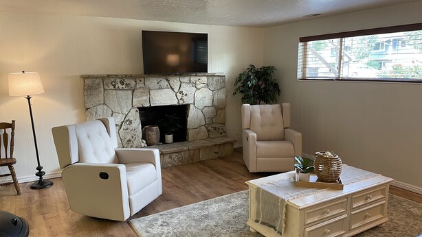 A living room with a stone fireplace, two white armchairs, a coffee table, and a lamp. - Newly Renovated Mother-in-Law Apartment (Orem)