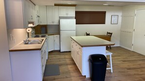 A compact kitchen with white cabinets, a built-in stove, a refrigerator, and a wooden dining table with chairs. - Newly Renovated Mother-in-Law Apartment (Orem)