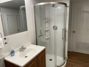 Un bany modern amb plat de dutxa tancat per vidre, un lavabo blanc amb dispensador de sabó i un mirall sobre el lavabo.