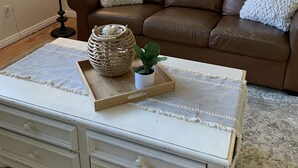 A living room with a brown leather sofa, a white coffee table with drawers, a floor lamp, a framed landscape painting, and a patterned rug. - Newly Renovated Mother-in-Law Apartment (Orem)