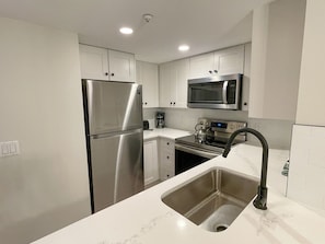 A modern kitchen with stainless steel appliances, a sink, and white cabinetry.