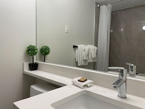 A modern bathroom with a marble sink, a mirror, a shower curtain, and a small potted plant. - Stoney Creek Northstar 20 (Whistler)