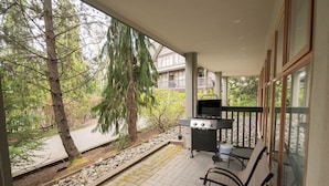 A covered patio with a grill, seating, and a view of a wooded area. - Modern, Deluxe Stoney Creek Northstar Condo. Pool & Hot Tub, Gas Fireplace (Whistler)