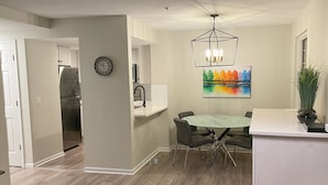 A modern kitchen with a built-in oven, a dining area with a round table and chairs, a clock on the wall, and a colorful painting above the sink. - Modern, Deluxe Stoney Creek Northstar Condo. Pool & Hot Tub, Gas Fireplace (Whistler)