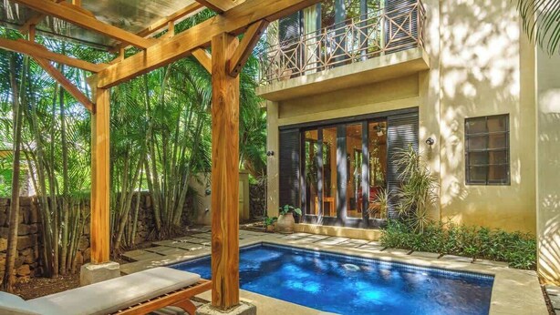 Ein Poolbereich mit einer Holz-Pergola, Liegestühlen und einer Steinmauer.