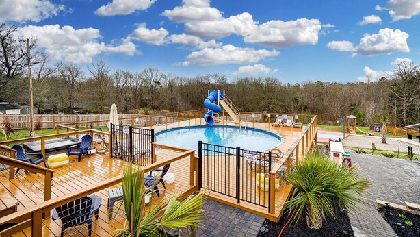 A pool area with a slide, deck chairs, and a fenced pool.