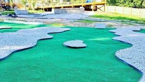 A green artificial turf play area with pebble borders and a central circular feature.