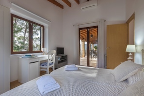 A bedroom with a bed, a desk, a chair, a TV, and a view of the outdoors.