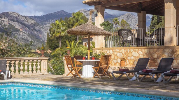 Ein Poolbereich mit Tisch und Stühlen, einem Reetdachschirm und Liegestühlen.