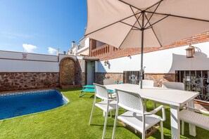 A pool with a stone wall, a white table with chairs, and a large umbrella. - Apartment Casa Patricia Nerja with Mountain View, Pool (Nerja)