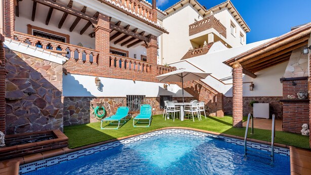 A swimming pool with a tiled border, surrounded by a stone wall and a brick building with a balcony. - Apartment Casa Patricia Nerja with Mountain View, Pool (Nerja)