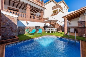 A swimming pool with a tiled border, surrounded by a stone wall and a brick building with a balcony. - Apartment Casa Patricia Nerja with Mountain View, Pool (Nerja)