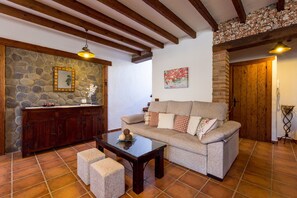 A living room with a stone wall, wooden beams, a sofa, a coffee table, and a cabinet. - Apartment Casa Patricia Nerja with Mountain View, Pool (Nerja)