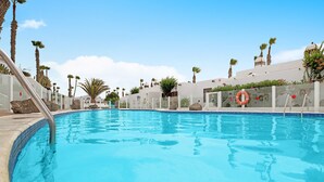 Une piscine à l’eau d’un bleu cristallin, entourée de palmiers et délimitée par une clôture blanche.