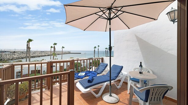 Un balcon avec vue sur la mer, une table avec une bouteille et des chaises longues.