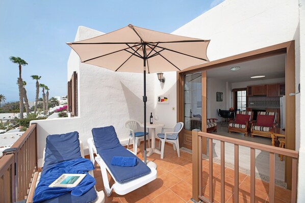 A balcony with two sun loungers, a table with chairs, and a large umbrella.