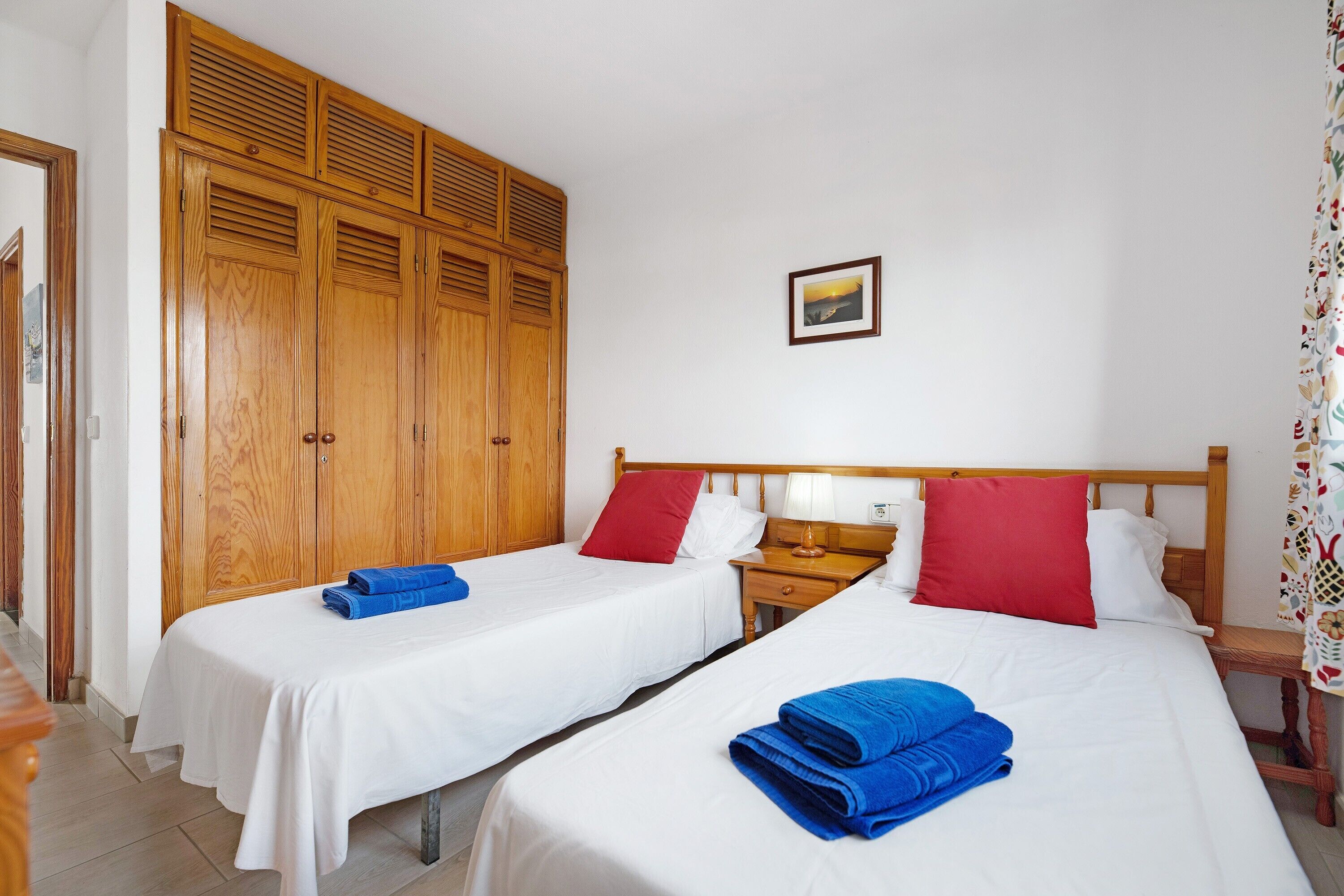 A hotel room with two beds, wooden wardrobes, a nightstand, and a small table.