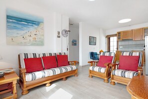 A living room with a sofa, chairs, a table, and a painting of a beach scene.