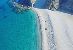 Vista aerea di una spiaggia con acque cristalline turchesi, formazioni rocciose e una riva sabbiosa.