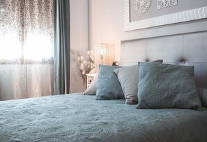 Una camera da letto con un letto, cuscini, un comodino, una lampada e un elemento decorativo a parete.