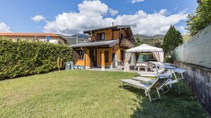 Ein zweistöckiges Haus mit Balkon, überdachter Sitzgelegenheit und Rasenfläche.