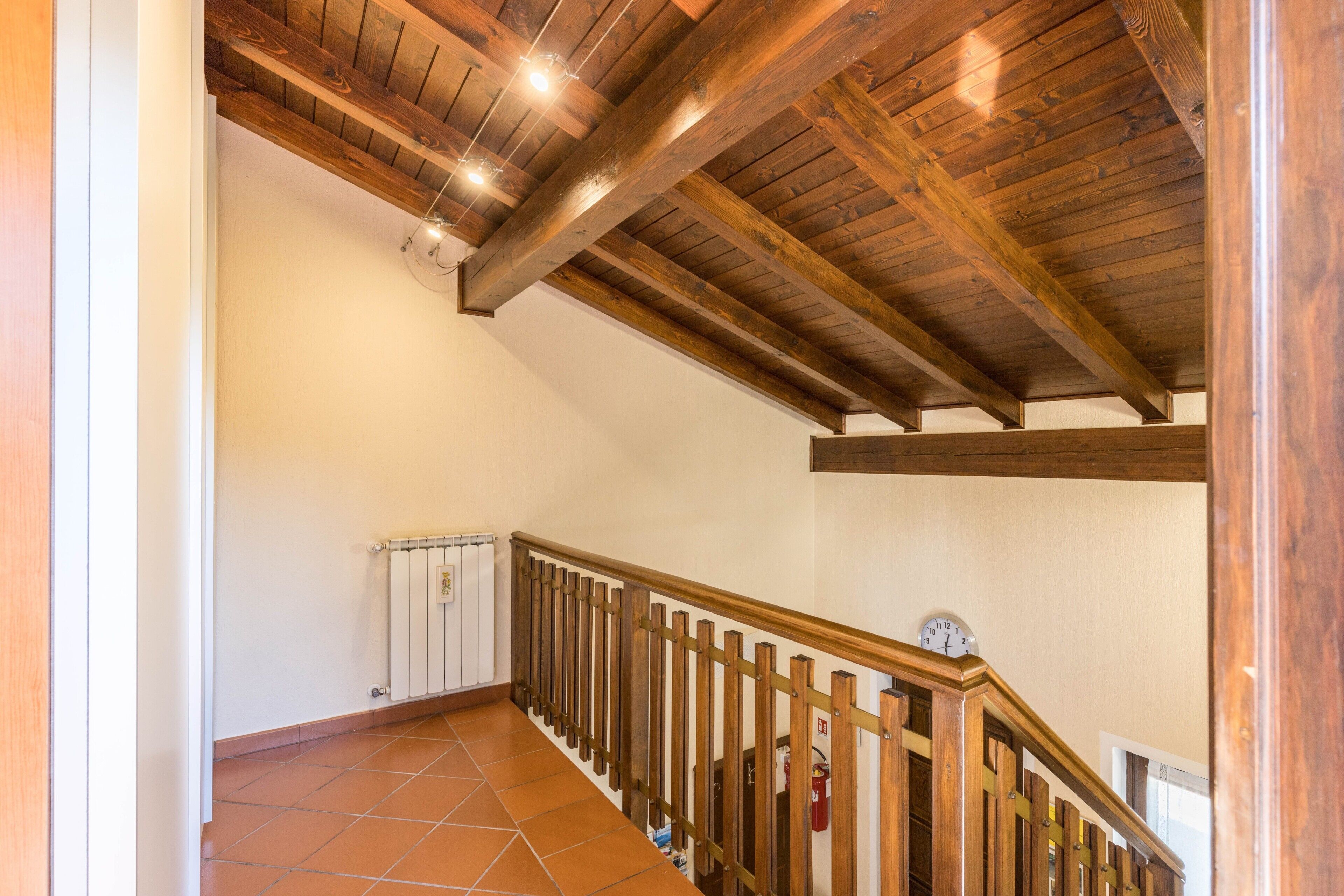 Eine Holztreppe mit Geländer, einem Heizkörper und einer Uhr an der Wand.