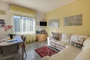 A living room with a sofa, a dining table with chairs, a TV, a map on the wall, and a window with curtains. - Casa Vacanza Elena: Family Paradise with Garden, Private Parking, Pet-Friendly, Val Grande View (Santino VB)